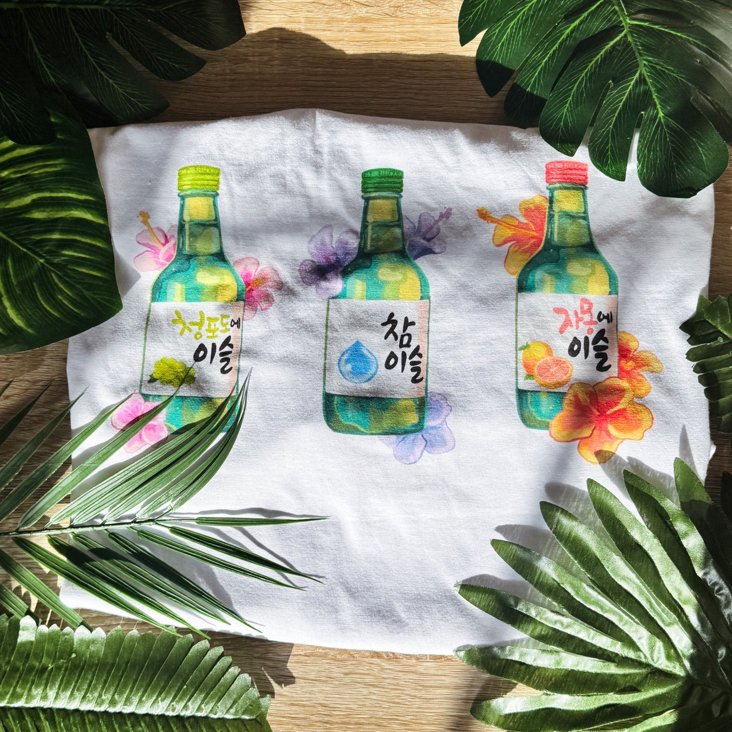 Three illustrated bottles on a white t-shirt with green leaves around