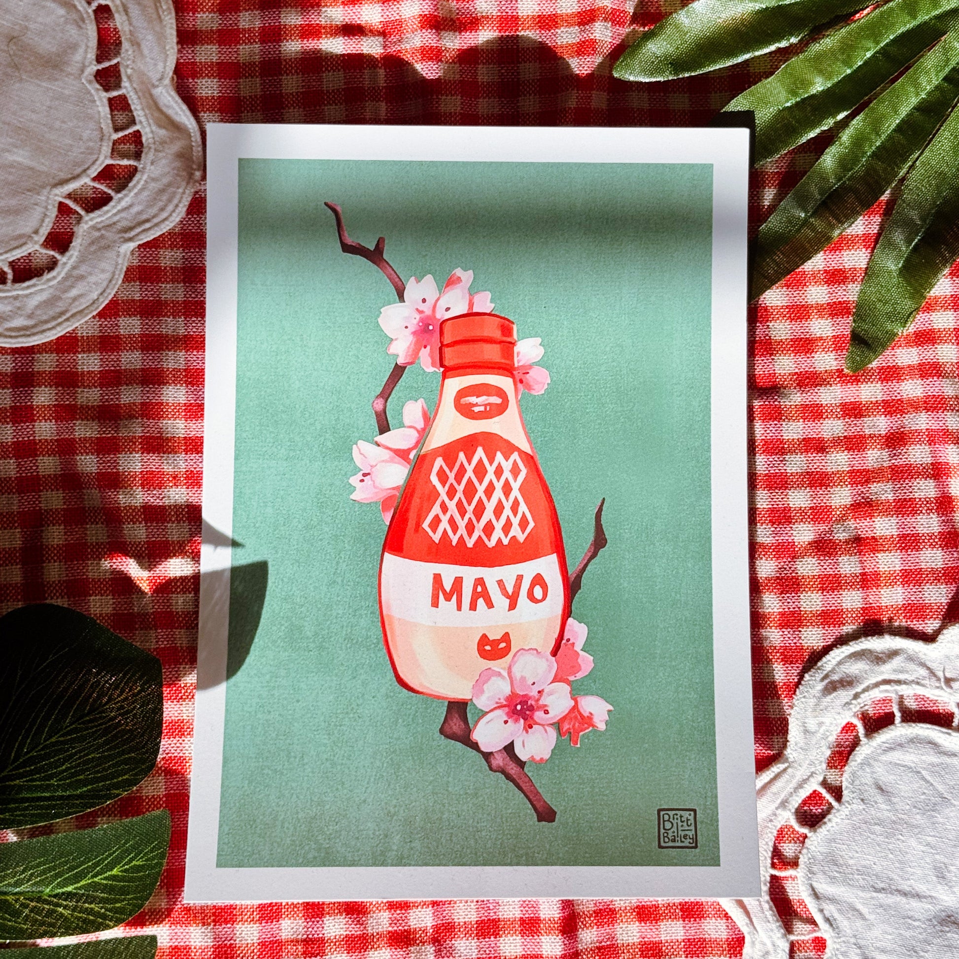 Framed artwork of a mayonnaise bottle with cherry blossoms on a red and white checkered tablecloth.